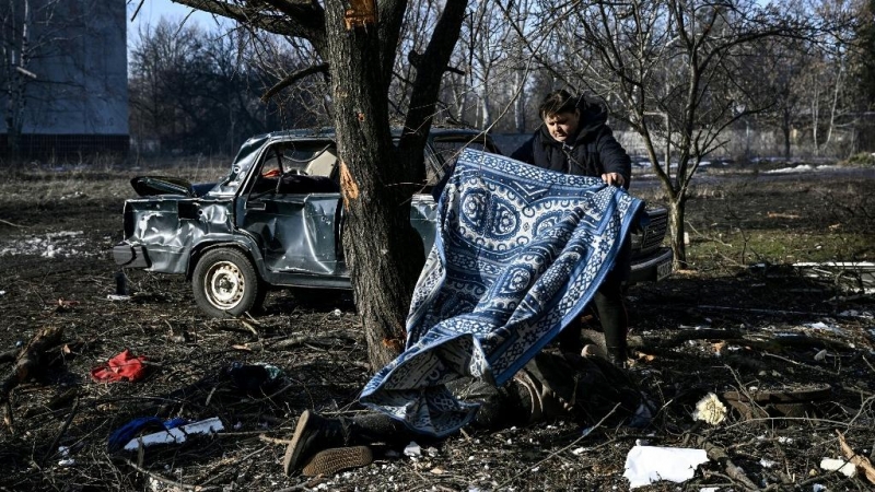 Un hombre usa una alfombra para cubrir un cuerpo tendido en el suelo después de los bombardeos en la ciudad de Chuguiv, en el este de Ucrania, el 24 de febrero de 2022, mientras las fuerzas armadas rusas intentan invadir Ucrania desde varias direcciones.