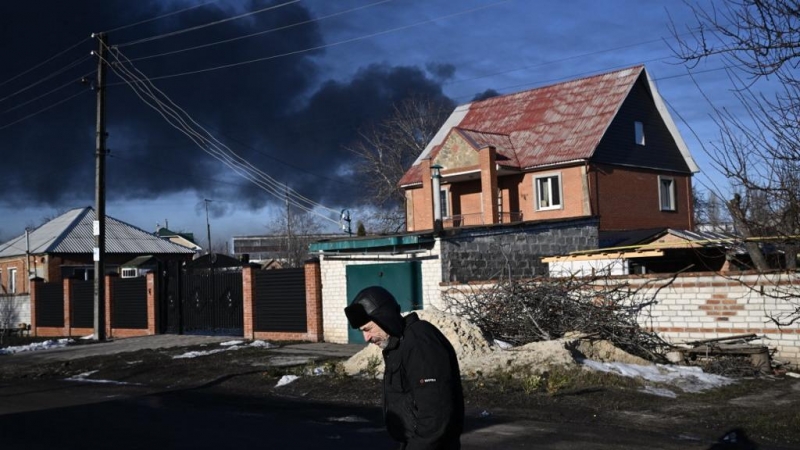 Un hombre camina en una calle mientras sale humo negro de un aeropuerto militar en Chuguyev, cerca de Kharkiv, el 24 de febrero de 2022.