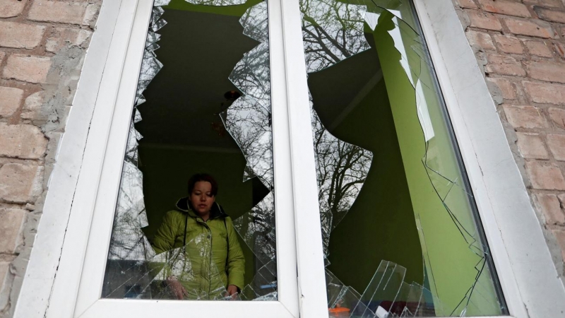 Una mujer mira a través de los cristales de su ventana, rotos por los recientes ataques bombardeos rusos en la ciudad de Yasynuvata (Yasinovataya), controlada por los separatistas prorusos, en la región de Donetsk.