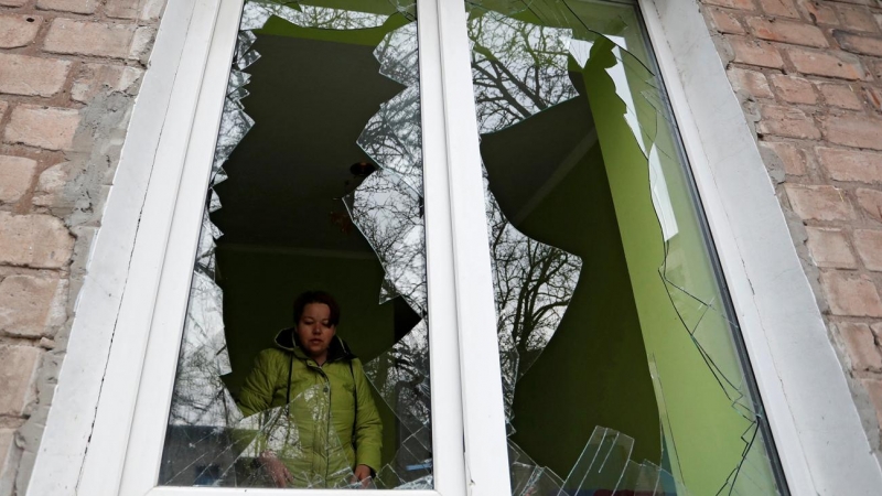 Una mujer mira a través de los cristales de su ventana, rotos por los recientes ataques bombardeos rusos en la ciudad de Yasynuvata (Yasinovataya), controlada por los separatistas prorusos, en la región de Donetsk.