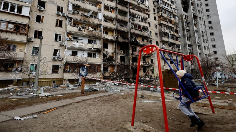 Un niño en un columpio frente a un edificio residencial dañado este viernes por la artillería rusa, en Kiev, Ucrania