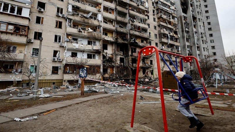 Un niño en un columpio frente a un edificio residencial dañado este viernes por la artillería rusa, en Kiev, Ucrania