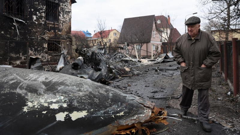 Un anciano camina entre los restos de un avión no identificado que se estrelló contra una casa en una zona residencial de Kiev, después de que Rusia lanzara una operación militar masiva contra Ucrania, este viernes 25 de febrero.
