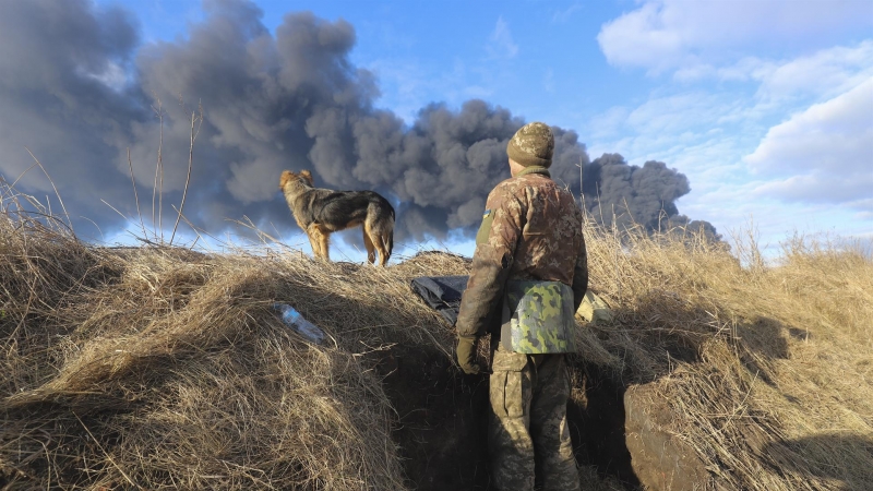 Un militar ucraniano y su perro se paran en una posición mirando el humo de un depósito de almacenamiento de petróleo quemado detrás después de que un misil ruso atacara cerca de Kiev, Ucrania, el 27 de febrero de 2022
