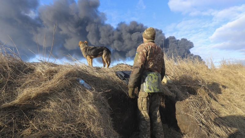 27/02/2022 Un militar ucraniano, junto a su perro, observa la columna de humo tras el bombardeo ruso a un depósito de petróleo cerca de Kiev