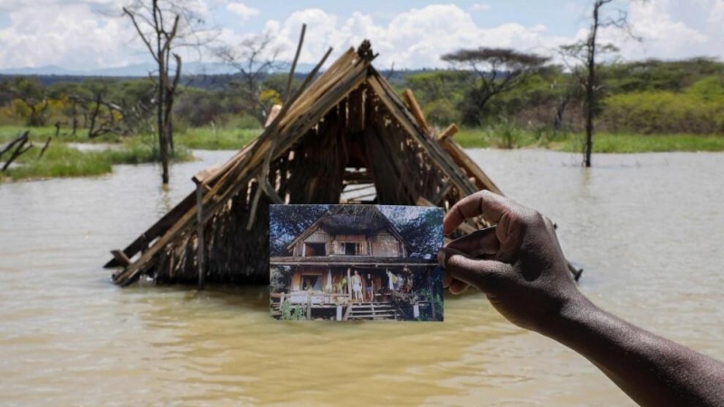 Un hombre sujeta una fotografía que muestra cómo era su hogar en Kenia antes de una inundación.