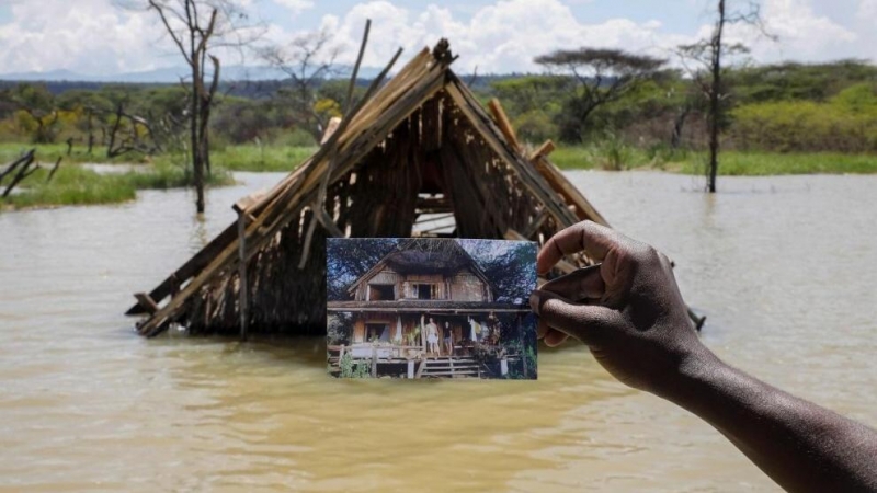 Un hombre sujeta una fotografía que muestra cómo era su hogar en Kenia antes de una inundación.