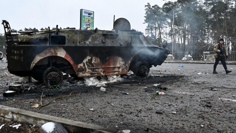 Un hombre armado pasa junto a un vehículo militar quemado en un puesto de control en la ciudad de Brovary, en las afueras de Kiev, este 1 de marzo. Las rusas llevarán a cabo un ataque contra la infraestructura de los servicios de seguridad de Ucrania en K