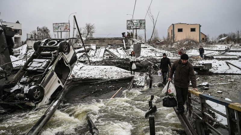 Varias personas cruzan un río cuyo puente ha sido destrozado en un bombardeo ruso, en la zona norte de Kiev. El Gobierno ucraniano ha insistido en que la defensa de la capital es 'prioritaria'.