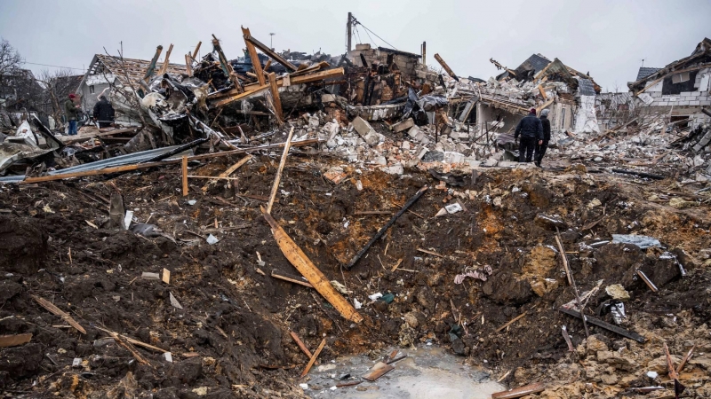 Las personas se paran sobre un cráter de proyectiles frente a los restos de un edificio residencial destruido por los bombardeos en Zhytomyr (Ucrania) este 2 de marzo de 2022.