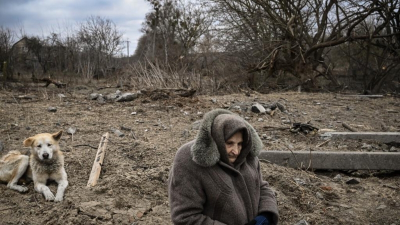 Una mujer se sienta mientras la gente cruza un puente cercano destruido mientras evacuan la ciudad de Irpin, al noroeste de Kiev, durante fuertes bombardeos y bombardeos el 5 de marzo de 2022.