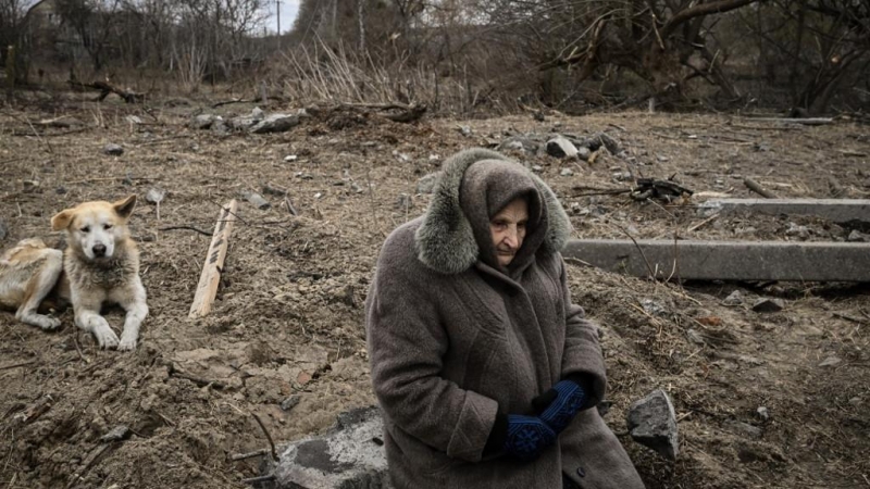 Una mujer se sienta mientras la gente cruza un puente cercano destruido mientras evacuan la ciudad de Irpin, al noroeste de Kiev, durante fuertes bombardeos y bombardeos el 5 de marzo de 2022.