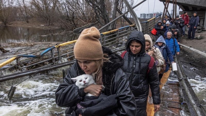 Una mujer con su gato cruza un puente destruido mientras los residentes huyen desde el frente de la ciudad de Irpín, en Kiev, este lunes 7 de marzo de 2022.