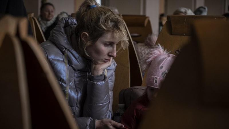 Anna entretiene con el teléfono móvil a su hija de 2 años, mientras espera a que llegue su tren en Odesa. Viene huyendo desde la ciudad de Mikolaev, bombardeada por los rusos desde hace varios días.