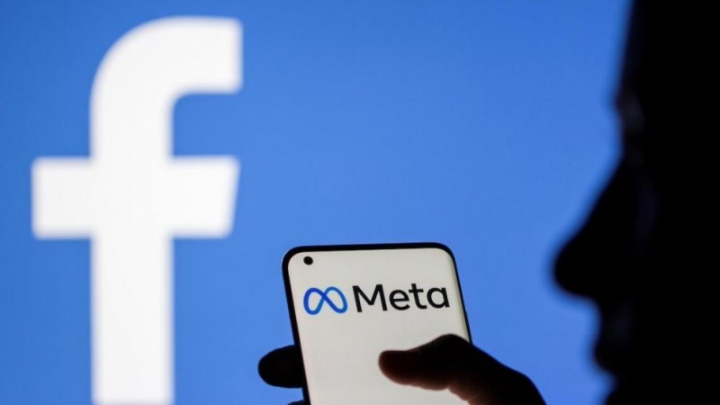 Una mujer sostiene un teléfono inteligente con el logotipo de Meta delante de la imagen de Facebook, a 28 de octubre de 2021.