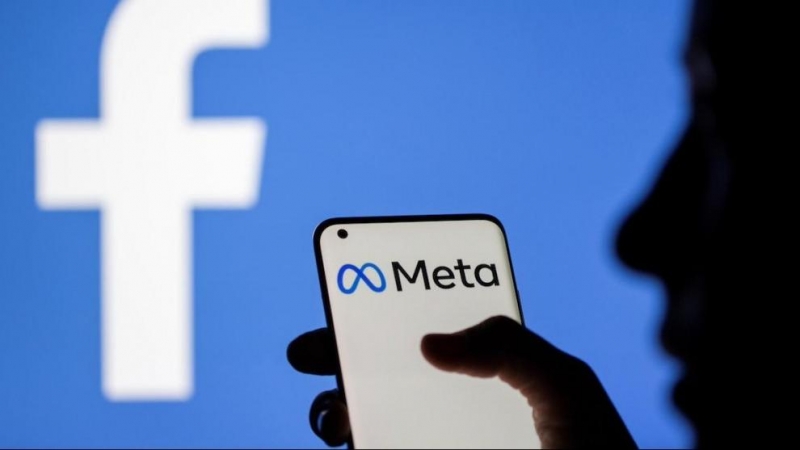 Una mujer sostiene un teléfono inteligente con el logotipo de Meta delante de la imagen de Facebook, a 28 de octubre de 2021.