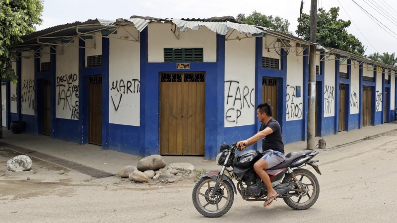 (19/02/2022)  Una persona mientras pasa en moto frente a varios grafitis de las FARC.