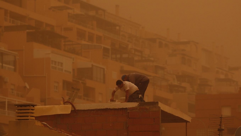 Unas personas trabajan en Aguadulce, Roquetas de Mar (Almería), que ha amanecido este martes bajo los efectos de una intensa calima.