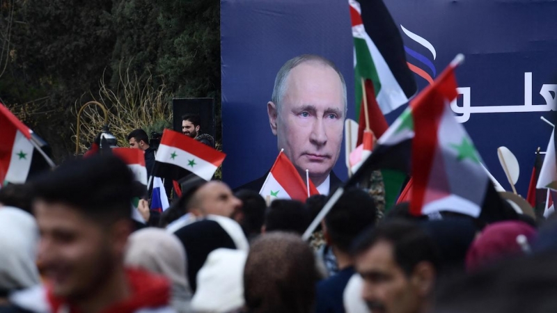 Estudiantes sirios ondean las banderas siria, rusa y palestina debajo de una valla publicitaria con el retrato del presidente ruso Vladimir Putin, en Alepo a 10 de marzo de 2022 .