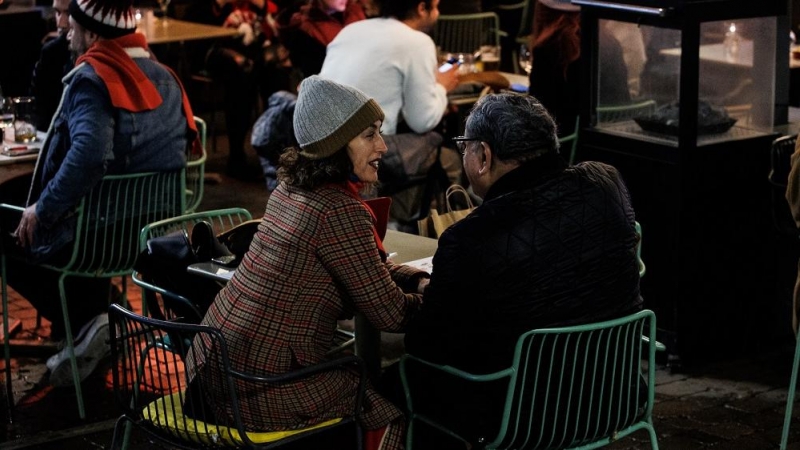 Dos personas en una terraza en la Plaza de Santa Ana para celebrar la llegada de la Nochebuena, a 24 de diciembre de 2021, en Madrid (España). A pesar de las nuevas restricciones, como el uso de la mascarilla en exteriores, que entra en vigor hoy, varias