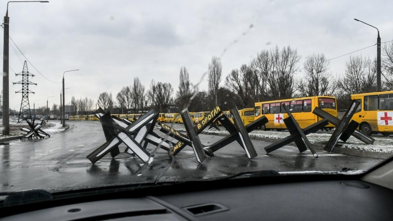 Obstáculos antitanque, conocidos como erizos checos, bloquean una calle cerca de un convoy de autobuses listos para despegar hacia la sitiada Mariupol para entregar ayuda humanitaria y evacuar a la gente.