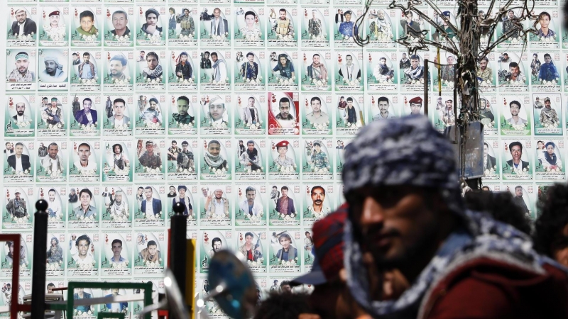 Los yemeníes se paran frente a una enorme pancarta que muestra los retratos de los combatientes hutíes presuntamente asesinados en el conflicto en curso, en una calle antes del séptimo aniversario de la campaña militar dirigida por Arabia Saudita en Yemen