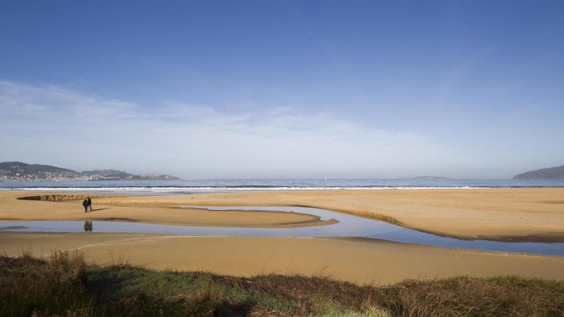 Dos personas pasean por la playa América en el ayuntamiento de Nigrán, Pontevedra.