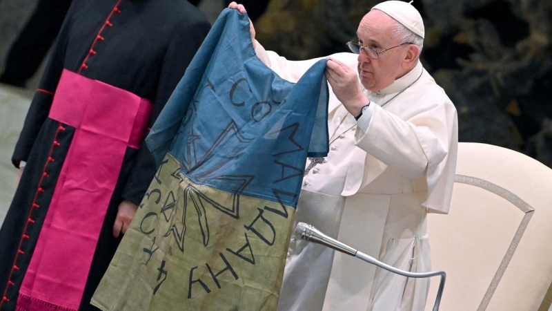 12/04/2022 - El papa Francisco muestra una bandera de Ucrania que fue enviada desde la localidad de Bucha durante la audiencia semanal en el Salón de Pablo VI en el Vaticano.