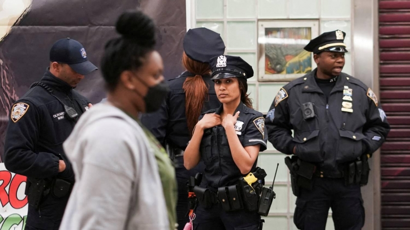 Una mujer pasa por delante de unos agentes de Policía en una estación de metro de Manhattan, desplegados tras el tiroteo registrado en Brooklyn este 12 de abril de 2022.