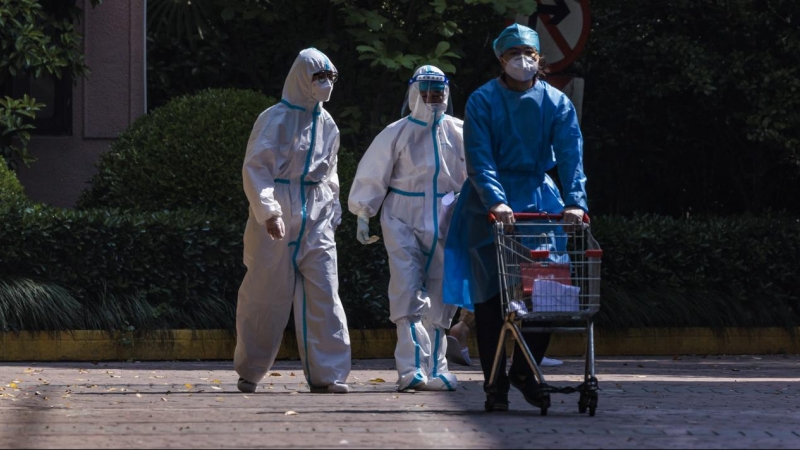 (12/02/2022) Trabajadores comunitarios caminan por una zona residencial con el traje de protección.