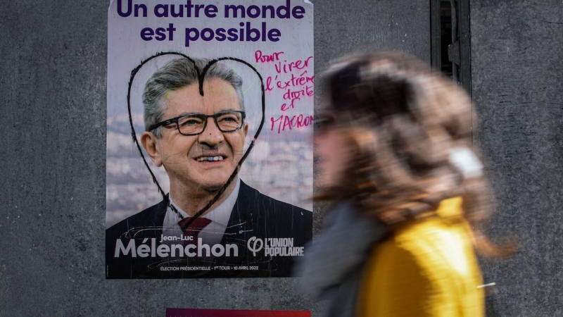 Una mujer camina en París el 9 de abril de 2022 frente a un cartel de campaña de La Francia Insumisa (LFI), partido liderado por Jean-Luc Mélenchon.