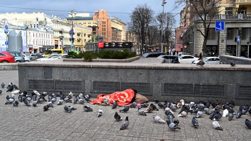 Un vagabundo duerme mientras las palomas se calientan junto a las rejillas de ventilación de un centro comercial subterráneo, centro de Kiev, a 9 de marzo de 2021.