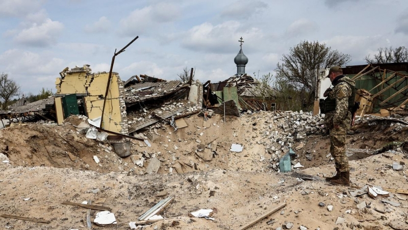 16/04/2022 Un militar ucraniano mira jacia un cráter y una casa destruida en la localidad de Yatskivka, en el este del país