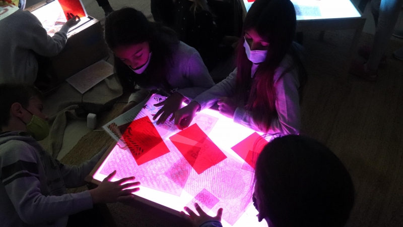 Plan abierto de un grupo de alumnos de la escuela del Bosque de la Pabordía de Girona trabajando los colores con una mesa con luz y papeles con mensajes escritos en diferentes colores el 2 de diciembre de 2021.