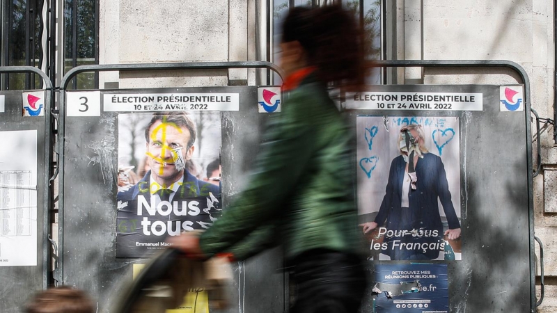 Una mujer camina junto a vallas publicitarias con carteles de los candidatos presidenciales franceses Macron y Le Pen, en París, Francia, el 18 de abril de 2022. Macron se enfrentará a la candidata del partido francés de extrema derecha Rassemblement Nati