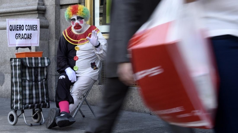 Rayito, un mendigo disfrazado de payaso, saluda sentado junto a un cartel que dice 'Quiero comer, gracias' en la calle Gran Vía, en el centro de Madrid, el 28 de octubre de 2014.