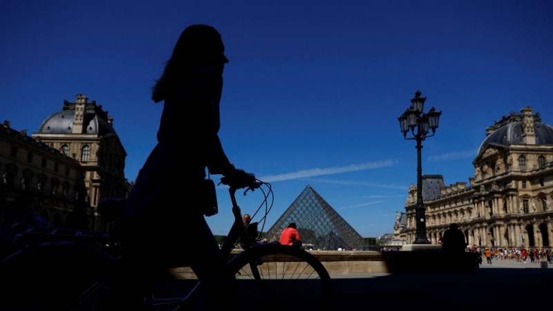11/05/2022-Una mujer camina con su bicicleta cerca de la Pirámide de cristal del museo del Louvre París, Francia, el 11 de mayo