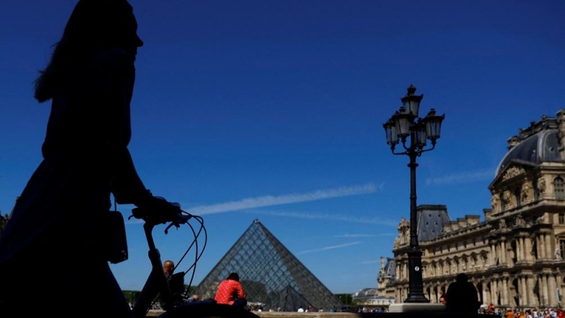 11/05/2022-Una mujer camina con su bicicleta cerca de la Pirámide de cristal del museo del Louvre París, Francia, el 11 de mayo