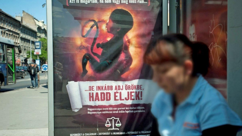 Una mujer espera junto a un cartel antiaborto con la imagen de un feto y el lema 'Puedo entender si aún no estás preparado para recibirme, ¡pero haz que me adopten y déjenme vivir!', en Budapest, a 17 de mayo de 2011.