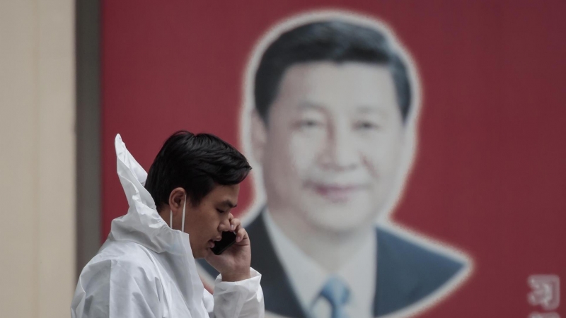 Un hombre con equipo de protección habla por teléfono en la calle, frente al cartel del presidente chino Xi Jinping, en medio del bloqueo de Covid-19 en Shanghái, China, el 23 de mayo de 2022.