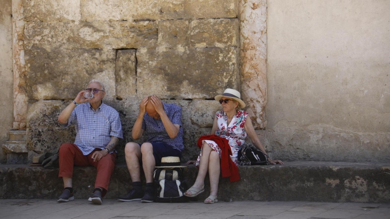 Unos turistas descansan y beben agua sentados a la sombra en los alrededores de la Mezquita-Catedral en Córdoba