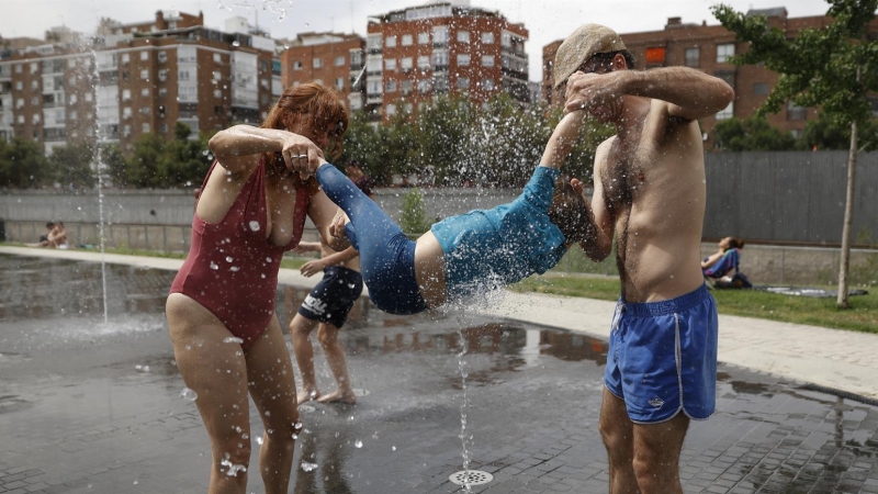 Una familia juega en la fuente de un parque en Madrid este domingo.