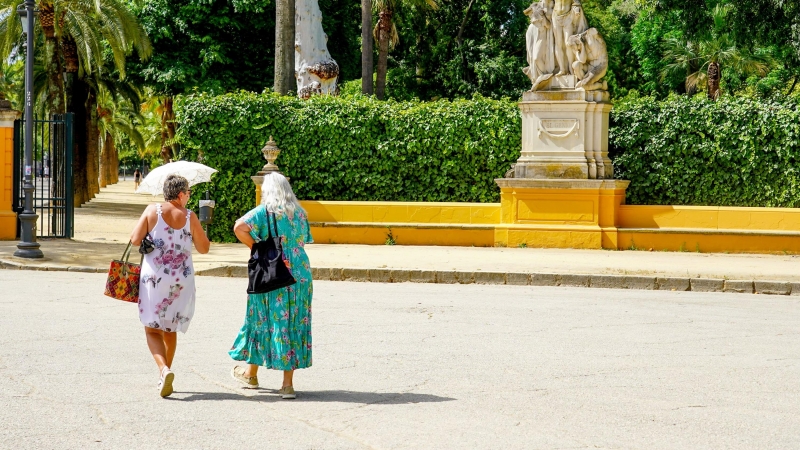 Dos mujeres con un paraguas pasean por el Parque de Maria Luisa en la primera ola de calor con temperaturas que sobrepasaran los 40 grados a 12 de junio del 2022 en Sevilla