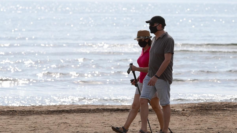 Dos personas protegidas con mascarilla pasean por la playa de la Malvarrosa durante su franja horaria permitida en la desescalada ante la crisis del Covid-19 en la que mayores de 14 años y menores de 69 tienen permitidas las salidas para pasear y hacer de