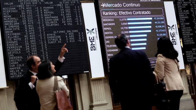 Cuatro personas frente a un panel de valores del Ibex 25 en el Palacio de la Bolsa, a 30 de mayo de 2022, en Madrid.