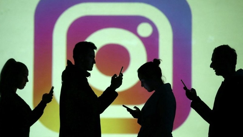 24/06/2022. Un grupo de personas usan sus teléfonos móviles en frente de una pantalla con el logotipo de Instagram, a 28 de marzo de 2018.