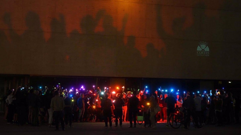 Un grupo de personas ilumina con linternas con colores de la bandera arcoiris la sede de las Cortes de Castilla y León, en Valladolid.