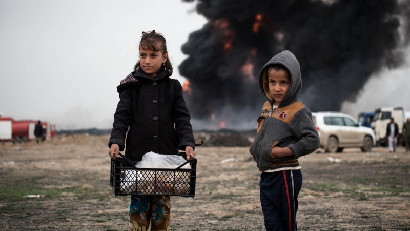 Niños llevan comida a los bomberos mientras intentan extinguir los pozos de petróleo incendiados por los miembros de ISIS mientras se retiraban, en Qayyara, Irak, el miércoles 15 de marzo de 2017.