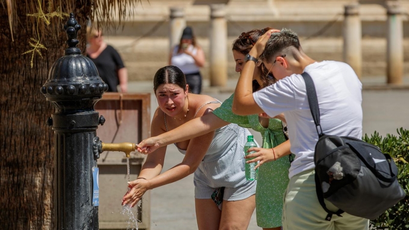Unas turistas se refrescan en una fuente de agua junto a la Catedral de Sevilla hoy viernes a mediodía.- EFE/Julio Muñoz
