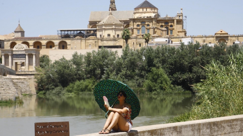 11/07/2022-Una turista se protege del calor con un paraguas y un abanico a la orilla del río Guadalquivir cerca de la Mezquita-Catedral de Córdoba este lunes cuando la Agencia Estatal de Meteorología (Aemet), ha alertado que la segunda ola de calor de est